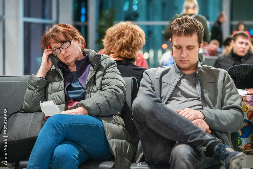 Tired man and woman are sitting in the waiting room of the international airport