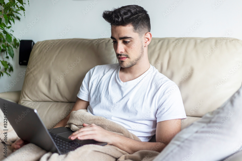 Young man relaxing on sofa while using laptop Young man relaxing on sofa while using laptop