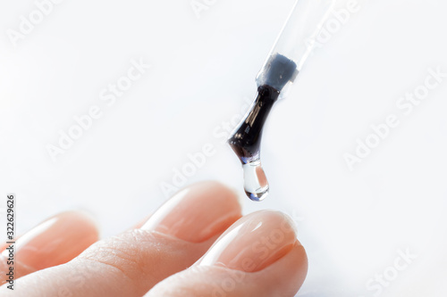 Macro photo manicure drop of varnish, master applies gel with brush on nails of girl white background