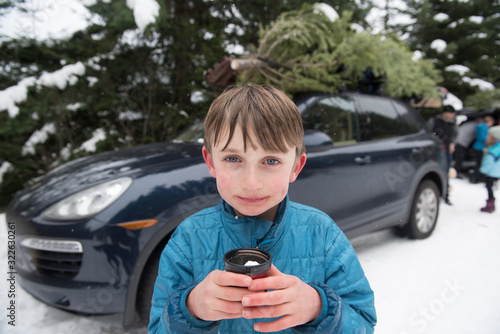 A boy holds a cup of hot chocolate after cutting a Christmas tree.
