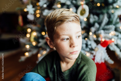 Young boy looking out window next to Christmas tree photo