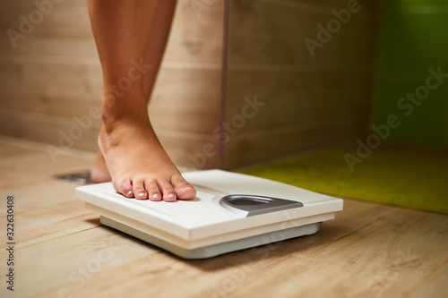 Woman weighing herself on weight scale in bathroom photo
