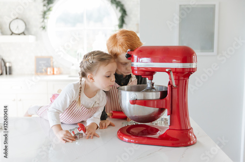 Two toddlers baking christmas cookies looking in a mixer