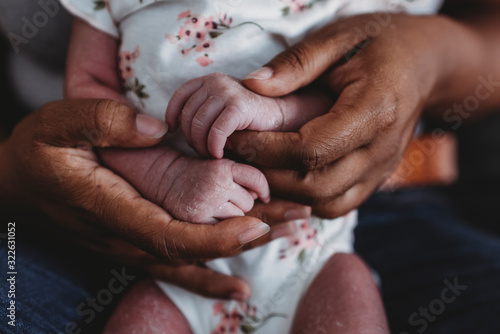 Ethnic female hands holding tiny waxy hands of multiracial newborn photo