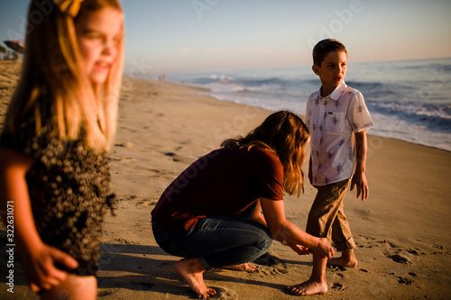 Mom Cuffing Son's Pants on Beach While Sister Waits photo