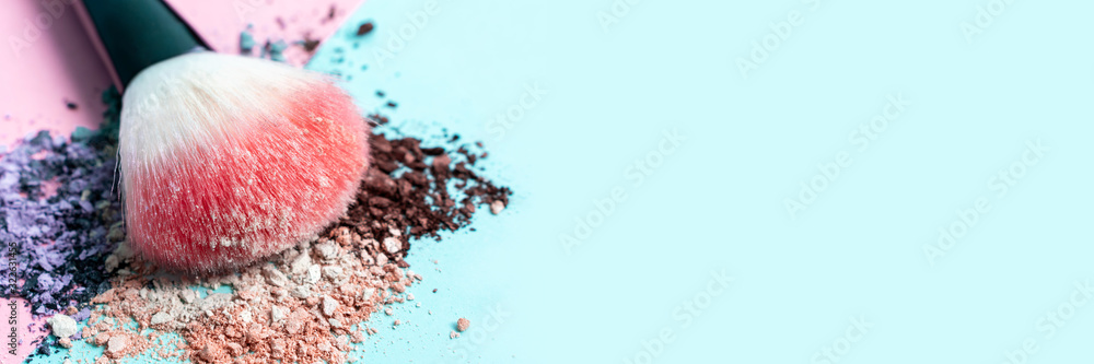 Beautiful bright makeup brush on a trendy pastel pink and blue background. Beauty banner. Cosmetic products. Crumbled multicolored eyeshadow. Place for text and design. Copy space. - obrazy, fototapety, plakaty 
