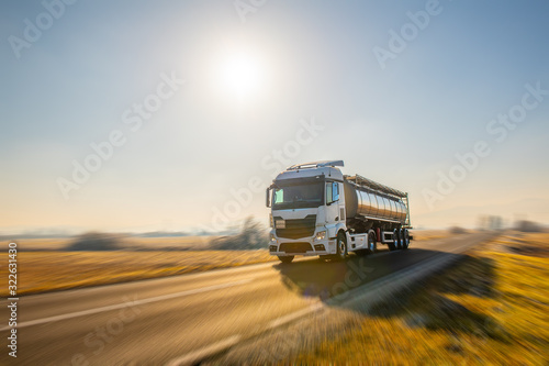 Close up of a fuel delivery truck driving by on an deserted ountry road on a beautiful sunny morning.