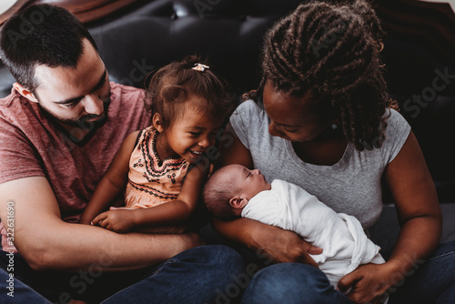 Multiracial parents holding smiling 2 yr old girl and swaddled baby photo