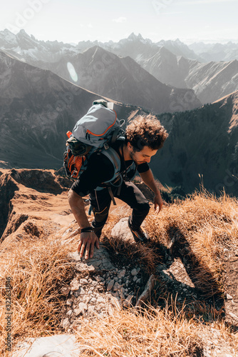 Young hiker climbing steep trail in front of alpine background photo