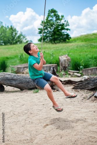 Boy 7-8 Years old swinging on tree swing laughing outdoors in summer photo