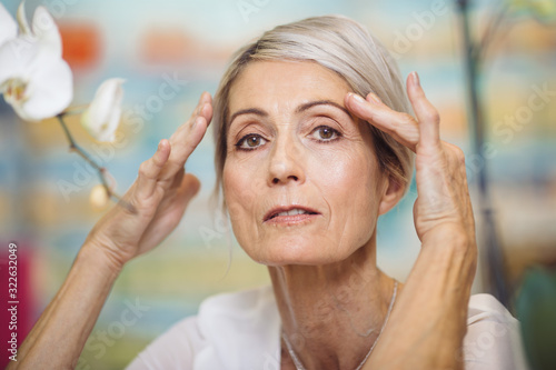 Portrait of 67 year old woman holding her hands near eyebrows photo