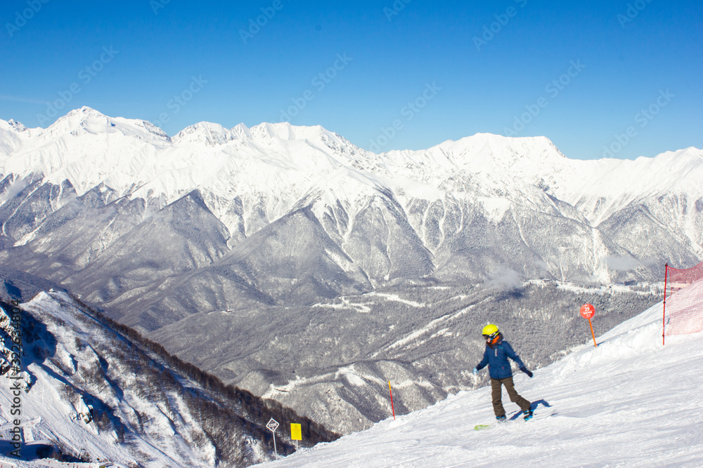 Beautiful view of the snowy mountain peak in the Alps with a snowboarder. Wonderful sunny weather. Sochi