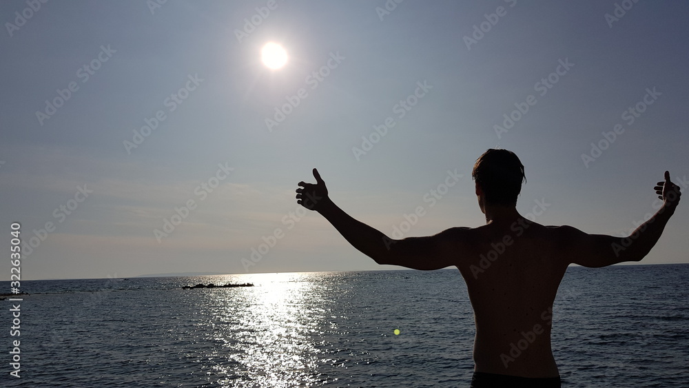 Silhouette of a young man standing on a boat and showing his muscles.