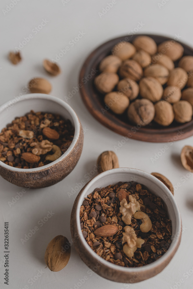 A healthy breakfast of granola, oatmeal, cereals, nuts. Bowls with granola, a plate with nuts on a white background. A healthy breakfast of granola, oatmeal, cereals, nuts. Bowls with granola, a plate with nuts on a white background.
