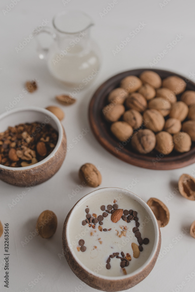 A healthy breakfast of granola, oatmeal, cereals, nuts and milk. Cups with granola, a jug of milk, a plate with nuts on a white background. A healthy breakfast of granola, oatmeal, cereals, nuts and milk. Cups with granola, a jug of milk, a plate with nuts on a white background.