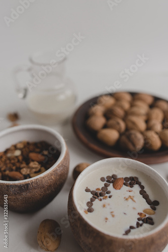 A healthy breakfast of granola, oatmeal, cereals, nuts and milk. Cups with granola, a jug of milk, a plate with nuts on a white background.