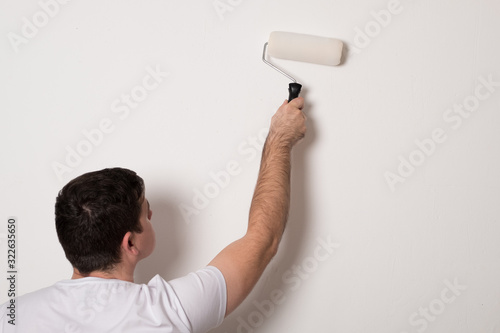 Man paints a wall with a roller. Young man paints a white wall.