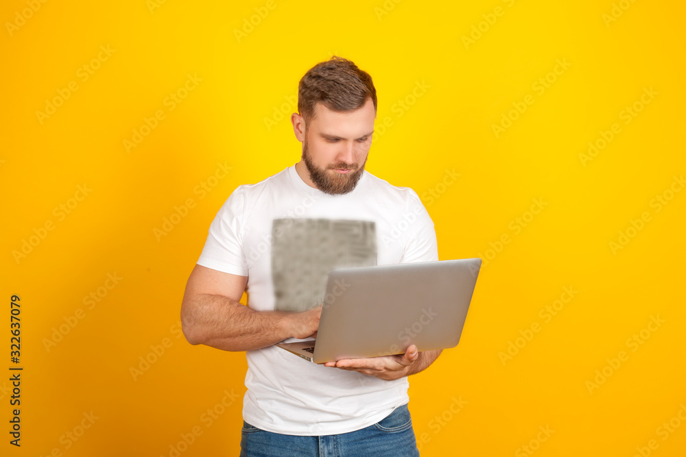 A man jokingly can't open a laptop, on a yellow background, in a white t-shirt and blue jeans, with copy space. Concept new modern technologies, gadgets and computer work. A man jokingly can't open a laptop, on a yellow background, in a white t-shirt and blue jeans, with copy space. Concept new modern technologies, gadgets and computer work.