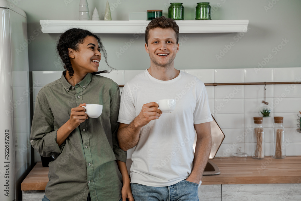 Obraz premium Mixed race couple. International friendship, happy time together, friends having relax time. Enjoy communication and holiday. Happy teenagers girl and guy laughing, drinking coffee on kitchen at home