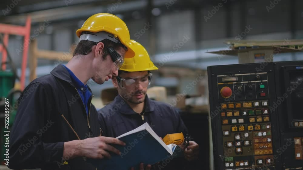 Couple technician men or factory workers try to fix the problem of the machine by use tools with manual book for helping in workplace industry area.