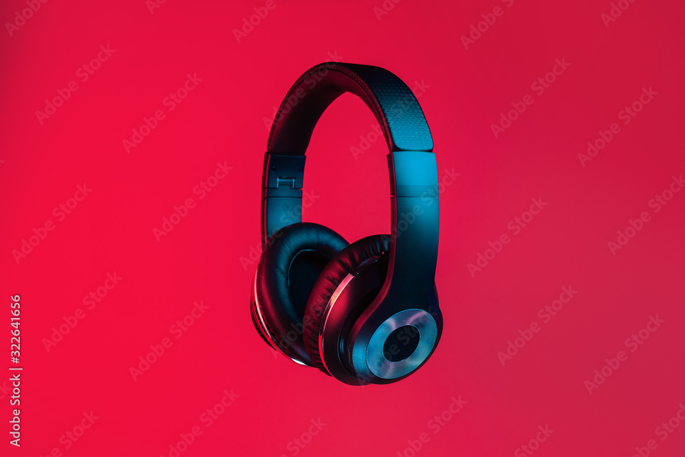 Retro 90s style photo of black stylish modern wireless headphone in neon lights over red background. Retro 90s style photo of black stylish modern wireless headphone in neon lights over red background.