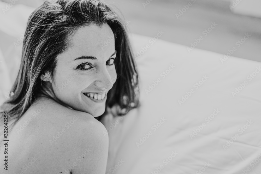 Naklejka premium young beautiful woman sitting on bed, resting and smiling. Lifestyle and beauty concept