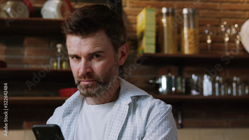 Close-up portrait of attractive confident man with beard standing in the middle of his kitchen. handsome guy n shirt looking on camera staying at home cooking breakfast.