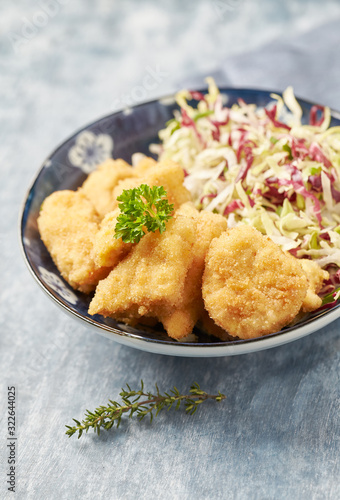 Chicken nuggets with raw salad and french fries on bright wooden background.