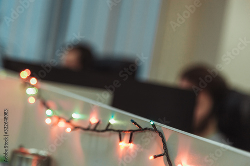 Christmas garland in the IT office. Two blurred programmers sitting at wotk