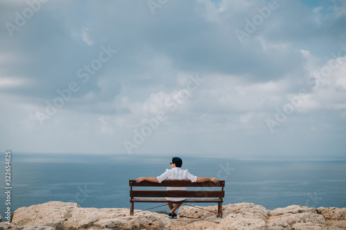 A man sits on a bench on the rocks overlooking the sea © Anna