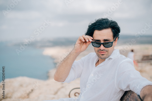 A man sits on a bench on the rocks overlooking the sea