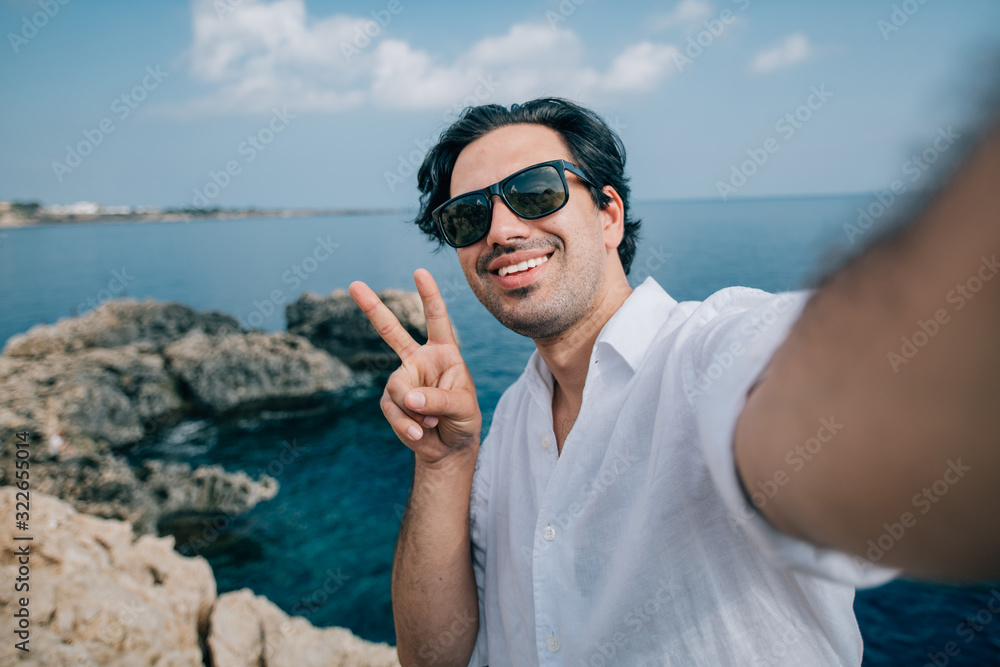 A man takes a selfie on the rocks with a sea view