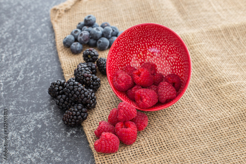 Mix of Red raspberries falling from a ceramic plate and a bunch of blackberries and blueberries in a rattan and black background. Stylish superfood photography