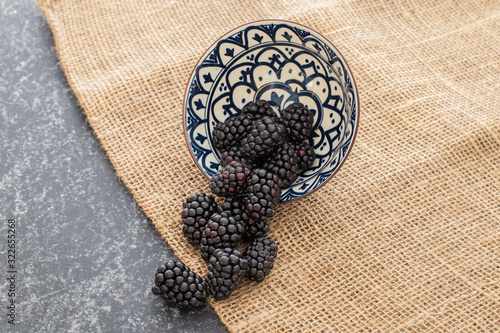 Blackberries falling from a ceramic plate in a rattan and black background. Stylish superfood photography. Top View