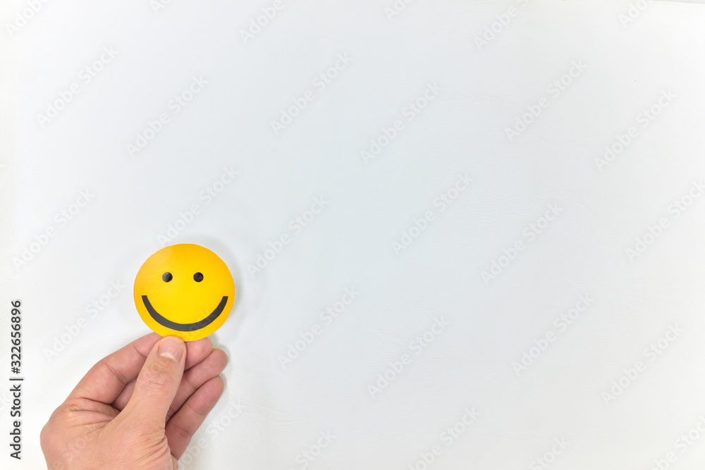 A hand hand holding a yellow smiley face on a white background. Positive feedback, satisfied customer and good service concepts
