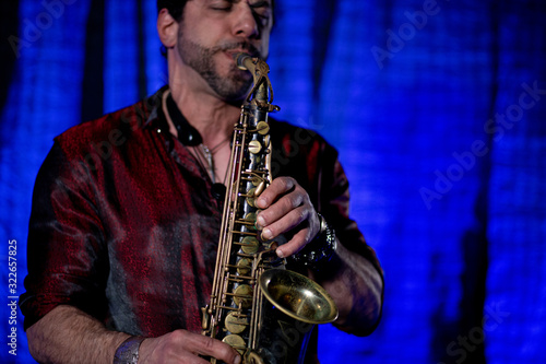 Saxophone player on blue blurred background. Saxophone in the foreground, blurred player. Close up