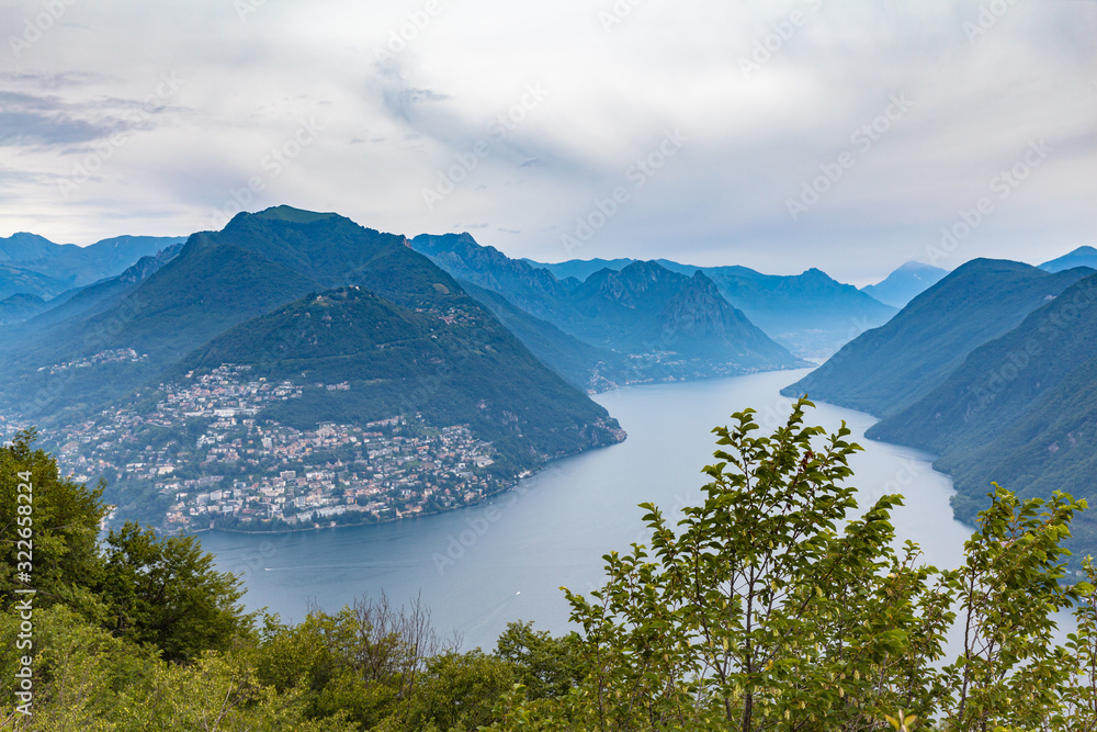Aerial panorama view of Lugano Lake, cityscape of Lugano, mountain Monte Bre and Swiss Alps mountain range on a cloudy summer day from top of Monte San Salvatore, Canton of Ticino, Switzerland