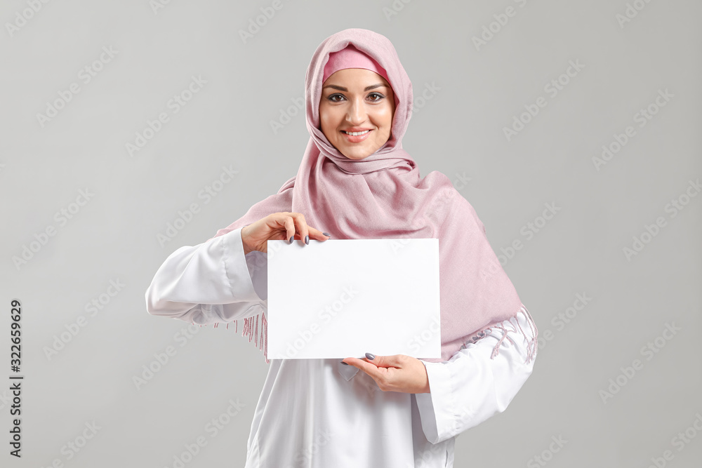 Young Arab woman with blank paper sheet on grey background Young Arab woman with blank paper sheet on grey background