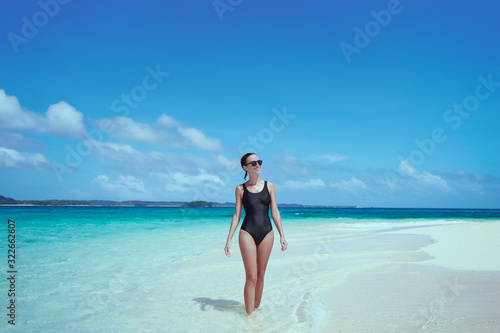 Vacation on the seashore. Back view of young woman walking on the beautiful tropical white sand beach. © luengo_ua
