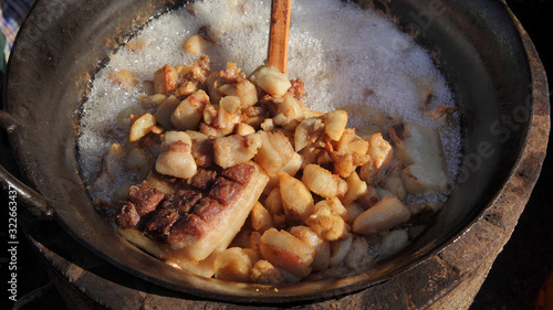 Pork greaves preparing in a big pot, tasty snacks in hot fat made from bacon