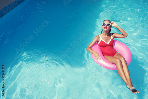 Enjoying suntan and vacation. Outdoor portrait of pretty young woman in red swimsuit with inflatable ring in swimming pool.