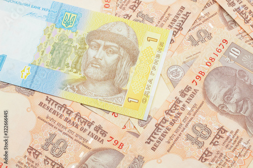 A blue and yellow one Ukrainian hryvnia bank note on a bed of Indian ten rupee bank notes photo