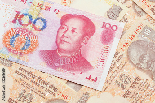 A close up image of a red, one hundred Chinese yuan bank note, close up on a background of orange Indian ten rupee bank notes. Shot in macro