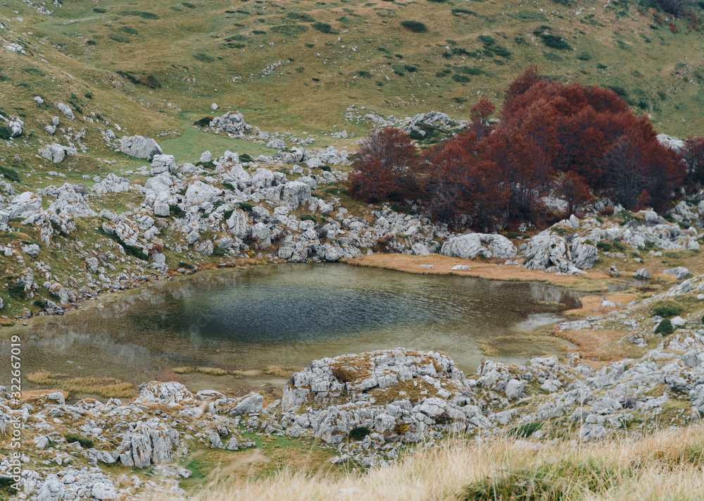 A small lake among a mountain range with red trees on the shore