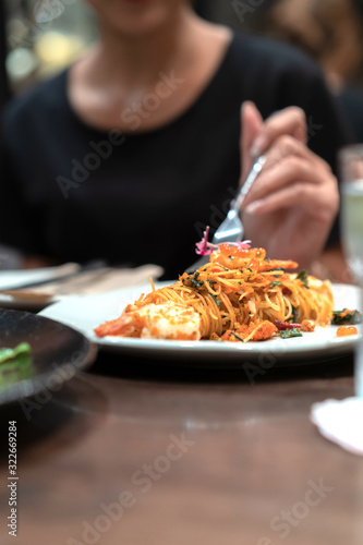 Close up and focus on the spaghetti noodle in the white dish white blur black dress female hand and her fork on it.