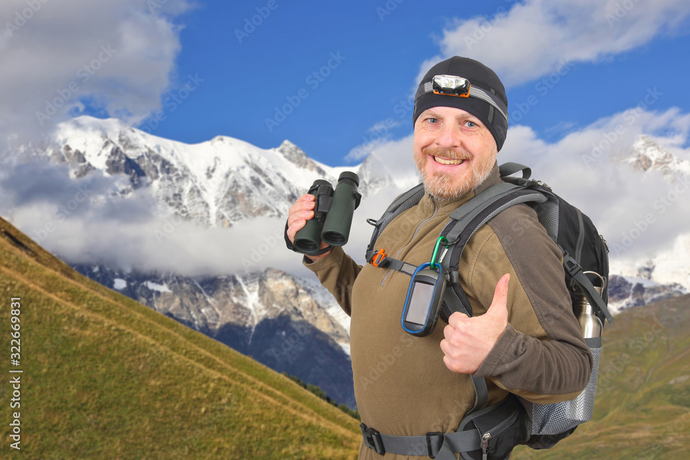 Happy man traveler with binoculars in hand on snow-capped mountains background