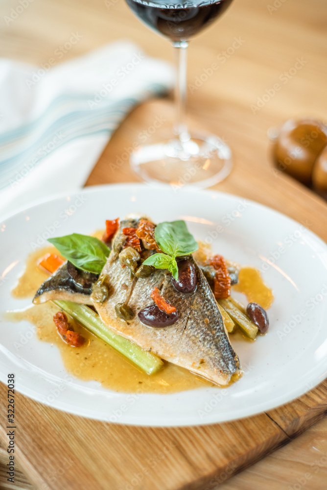 Grilled fish on white plate and wine glasses.