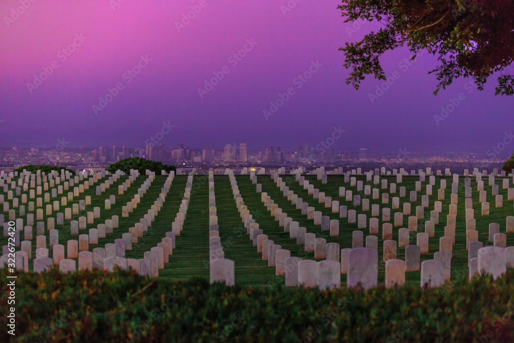 Obraz premium American war cemetery with rows of graveyard in Point Loma, California, United States with the skyscrapers of downtown San Diego on background. Twilight colorful sky.