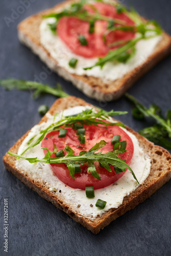 Healthy Breakfast Idea. Tomato sandwich with cream cheese and fresh rocket on black stone background.