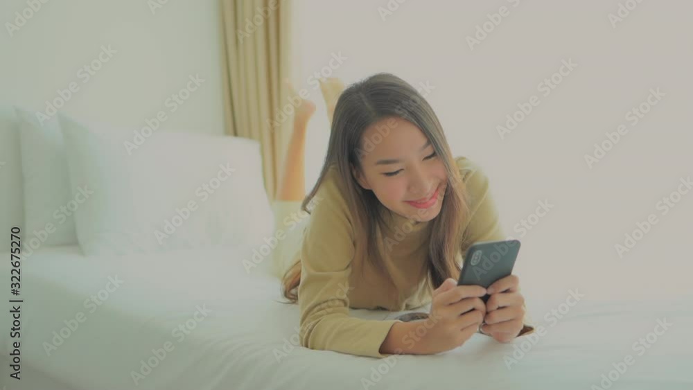 Beautiful Asian woman laying relaxed on the bed holding her Smartphone Beautiful Asian woman laying relaxed on the bed holding her Smartphone